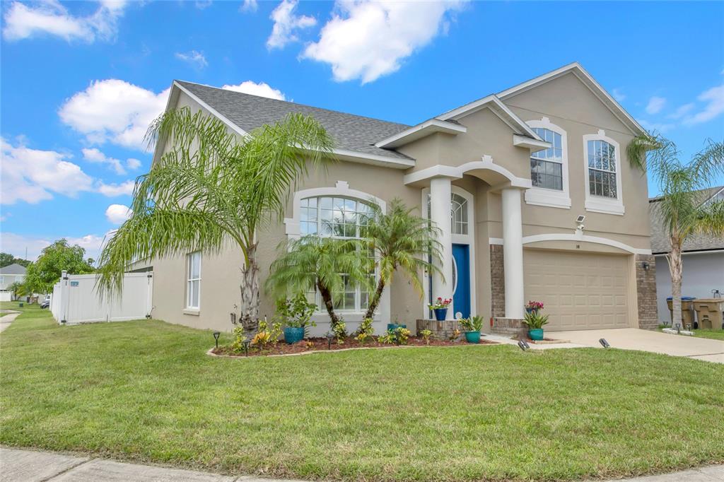 A two-story suburban house with a tan stucco exterior, a blue front door, and palm trees — 100 THORNBURY LANE, KISSIMMEE, FL