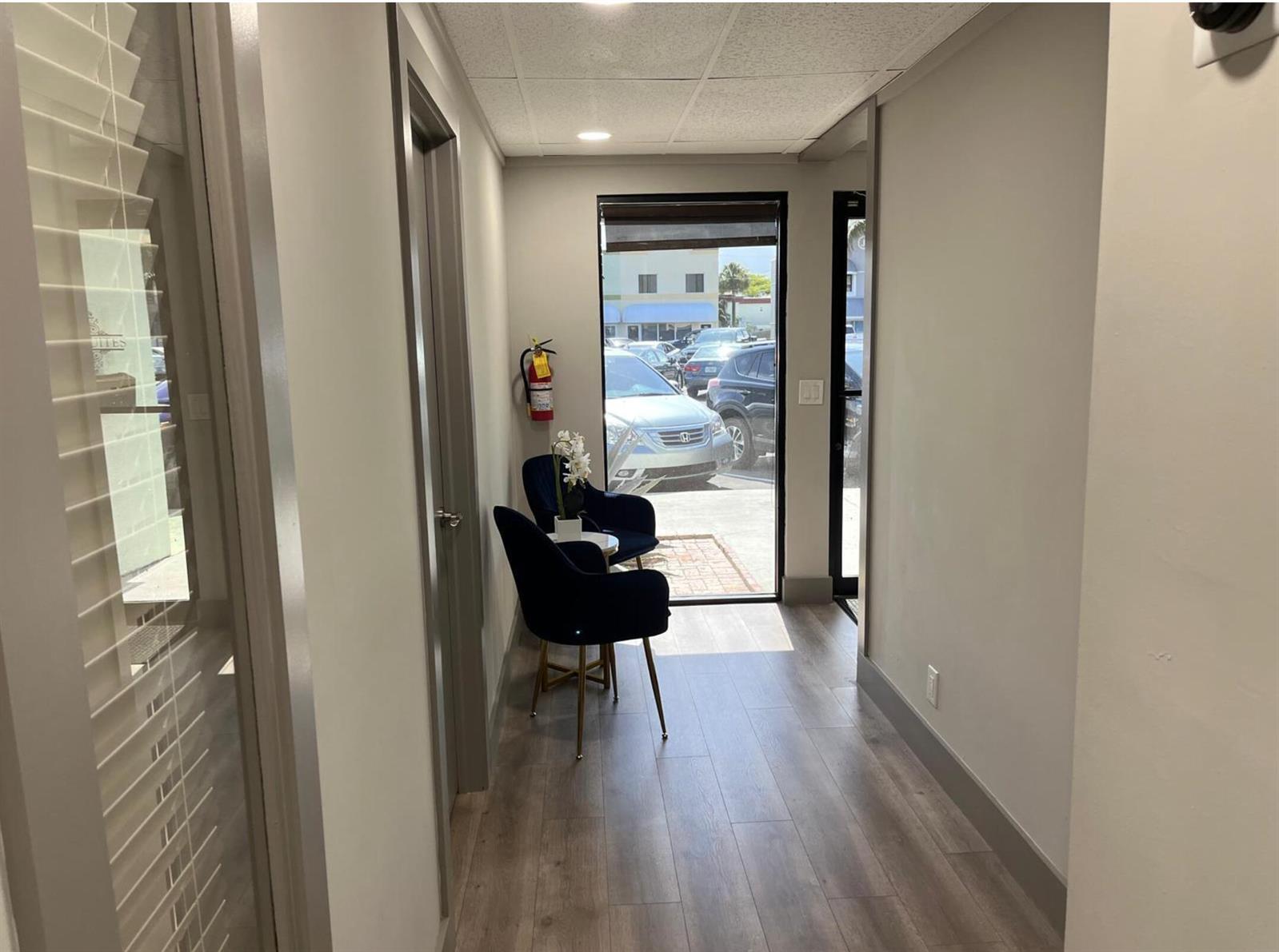 A hallway with wood-look flooring leads to an exterior glass door and two blue chairs — 828 SE 8th Avenue, Deerfield Beach FL 33441, DEERFIELD BEACH, FL