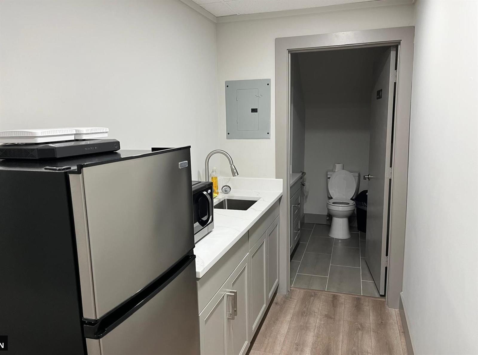 A kitchenette with a refrigerator and sink sits next to a doorway leading to a bathroom — 828 SE 8th Avenue, Deerfield Beach FL 33441, DEERFIELD BEACH, FL