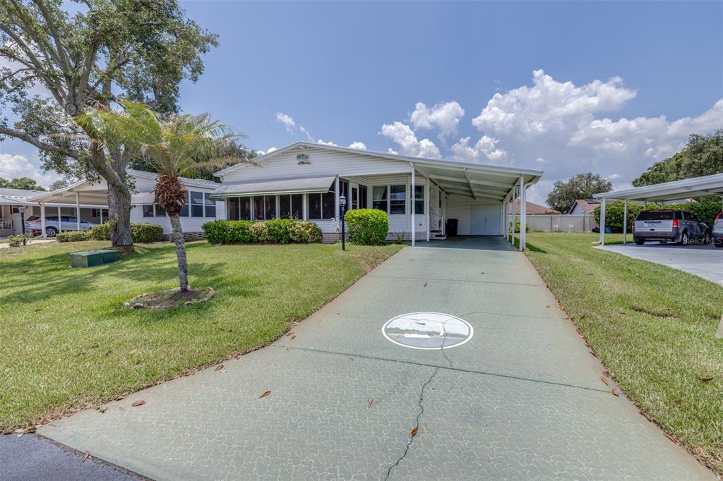 A single-story manufactured home features a green driveway, a carport, and a screened-in front porch — 6235 KNOTTY PINE DRIVE SE, WINTER HAVEN, FL