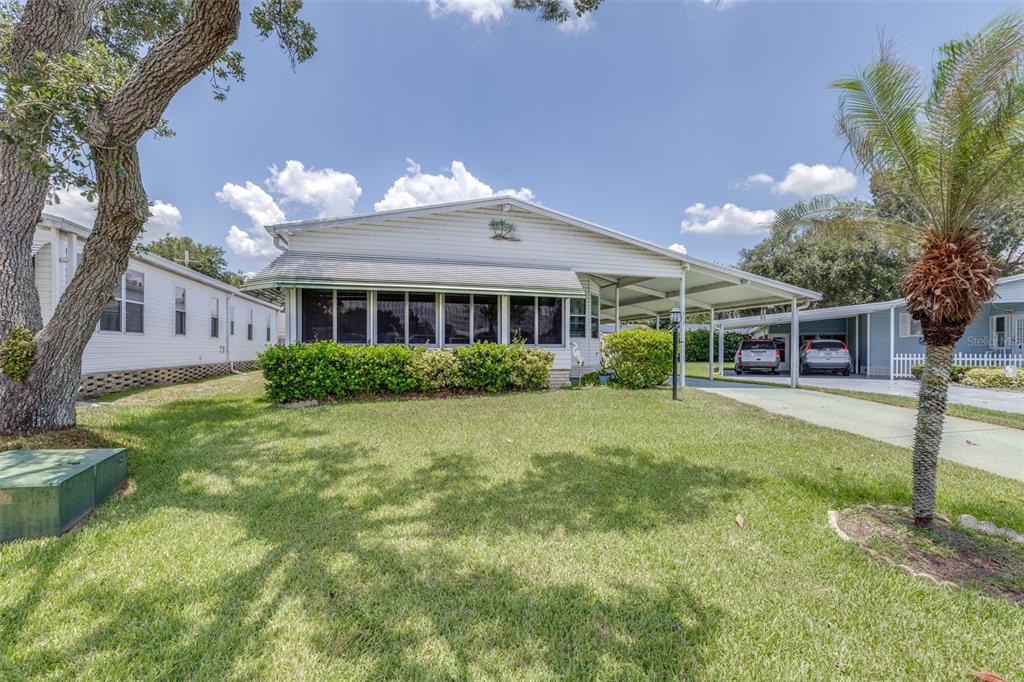 A single-story mobile home with a carport, a screened-in porch, and a grassy front yard — 6235 KNOTTY PINE DRIVE SE, WINTER HAVEN, FL