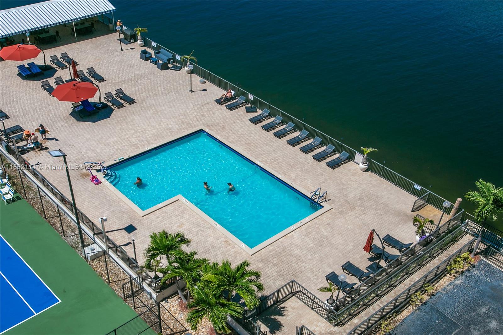 An aerial view shows a swimming pool on a paved deck beside a body of water — 2017 S Ocean Dr # 1008, Hallandale Beach FL 33009, HALLANDALE BEACH, FL