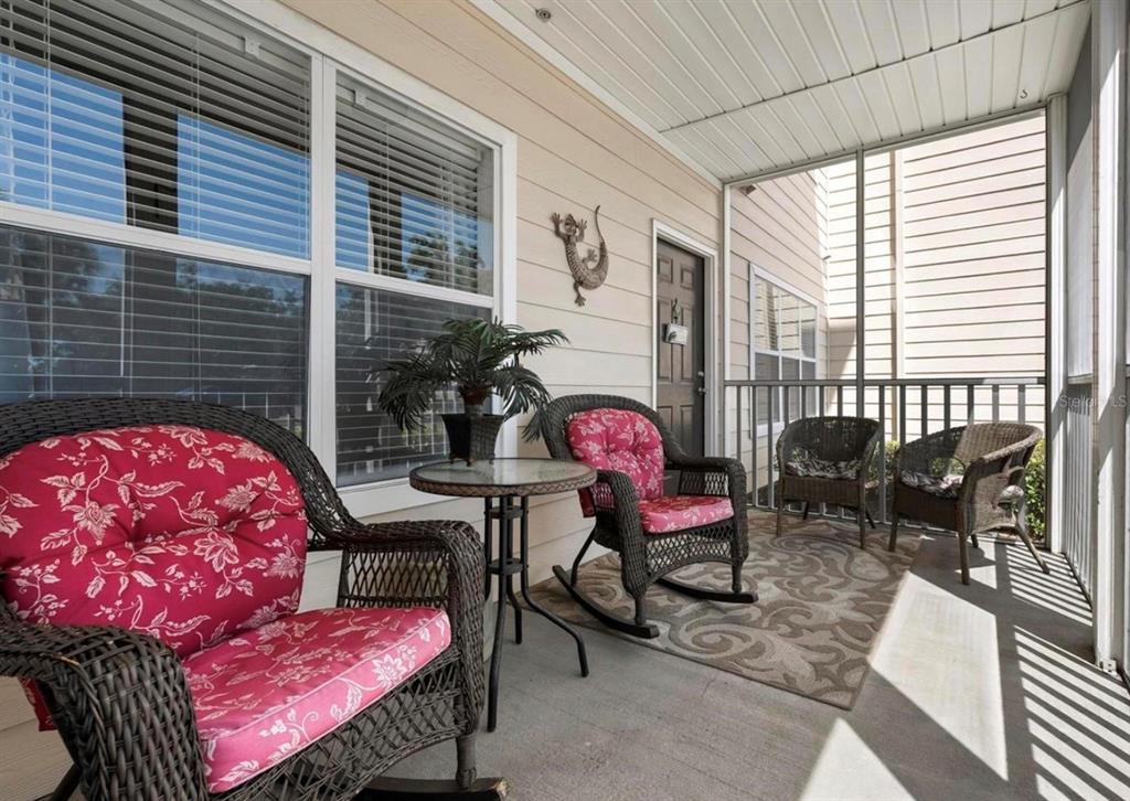 A screened-in porch features wicker rocking chairs with pink floral cushions and a small table — 4802 51ST STREET W UNIT 1908, BRADENTON, FL