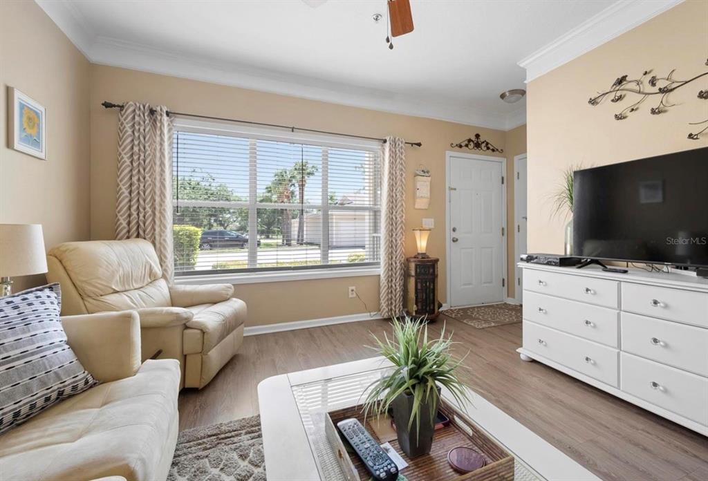 A living room features light-colored walls, wood-look flooring, a large window, and a white dresser — 4802 51ST STREET W UNIT 1908, BRADENTON, FL