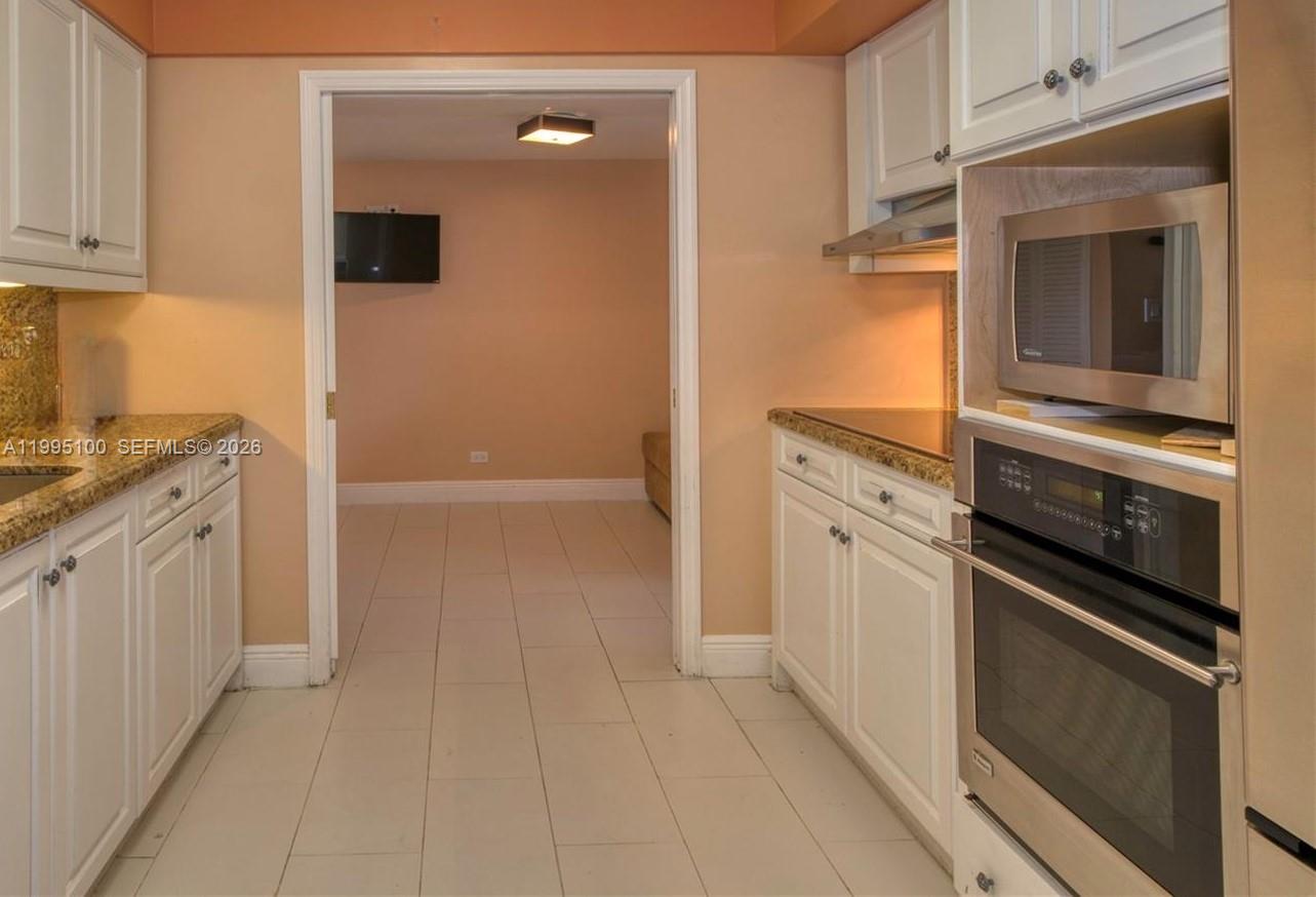 A galley-style kitchen features white cabinets, granite countertops, and a built-in oven and microwave — 1800 NE 114th St # 401, Miami FL 33181, MIAMI, FL