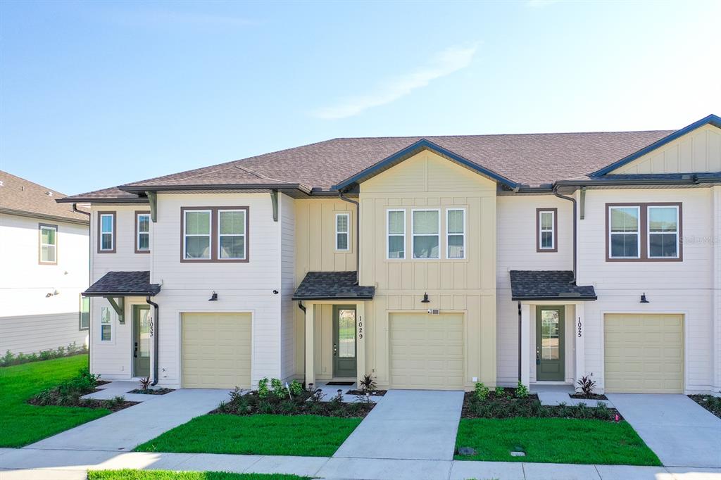 A row of three modern townhouses with garages, light-colored siding, and green front doors — 1029 PLANTATION LANE, DAVENPORT, FL