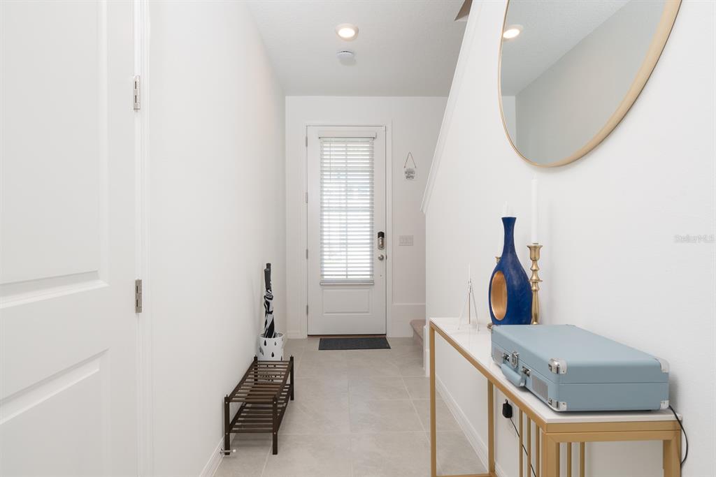 A bright entryway features a white door, tiled flooring, a console table, and a mirror — 1029 PLANTATION LANE, DAVENPORT, FL