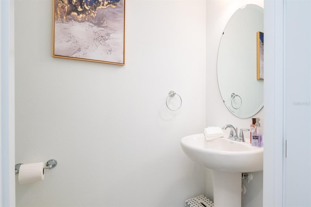 A small bathroom features a white pedestal sink, an oval mirror, and wall-mounted accessories — 1029 PLANTATION LANE, DAVENPORT, FL