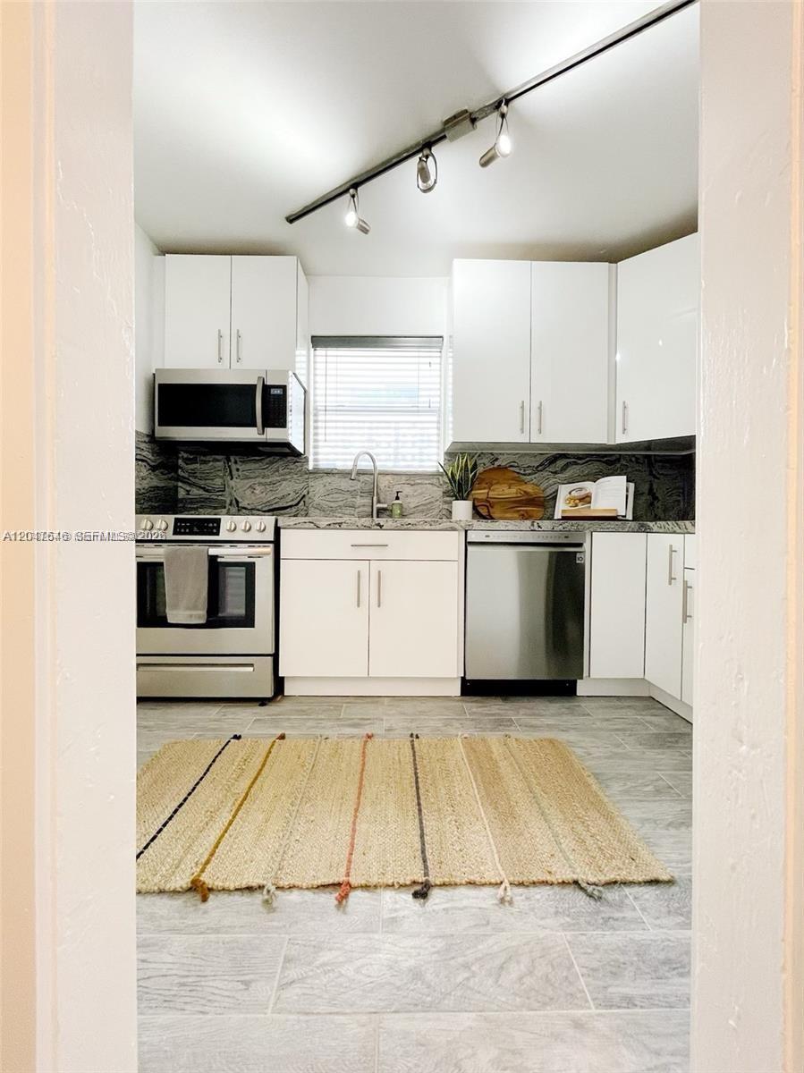 A kitchen features white cabinets, stainless steel appliances, a gray stone backsplash, and tile flooring — 1040 Lenox Ave # 1040, Miami Beach FL 33139, MIAMI BEACH, FL