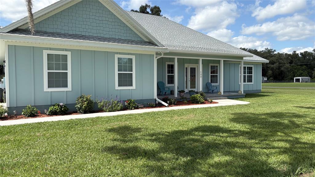 A light blue house with board-and-batten siding and a covered front porch sits on grass — 122 SW SCOTT PLACE, LAKE CITY, FL