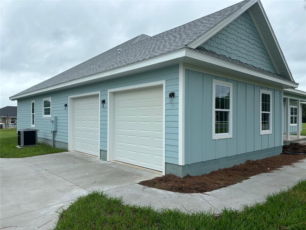 A light blue house exterior features two white garage doors and a concrete driveway — 122 SW SCOTT PLACE, LAKE CITY, FL