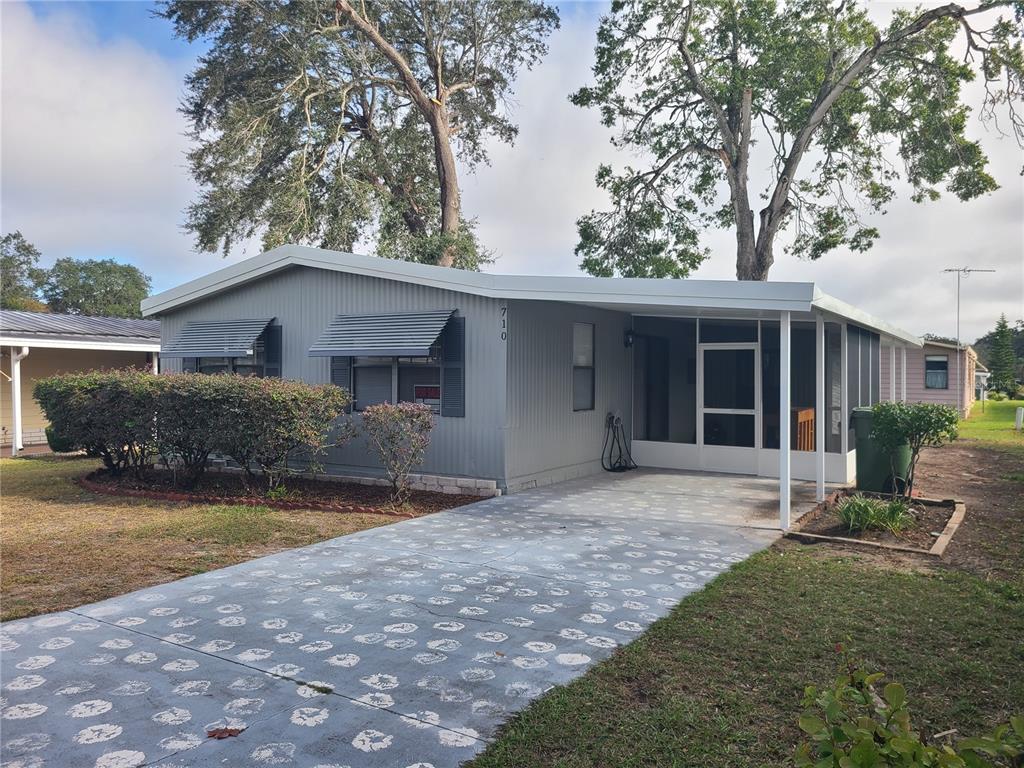 A single-story gray mobile home features a screened-in porch and a patterned concrete driveway — 710 COACHMAN DRIVE, LEESBURG, FL