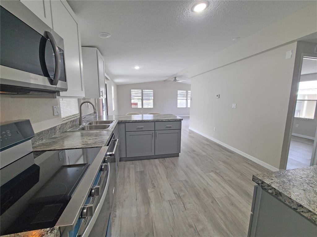 A kitchen with gray cabinets, granite countertops, and stainless steel appliances opens to a living area — 710 COACHMAN DRIVE, LEESBURG, FL