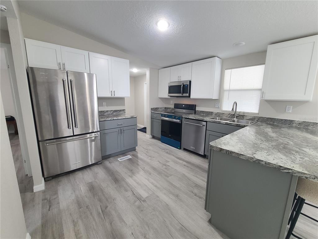 A kitchen features white upper cabinets, gray lower cabinets, stainless steel appliances, and granite countertops — 710 COACHMAN DRIVE, LEESBURG, FL
