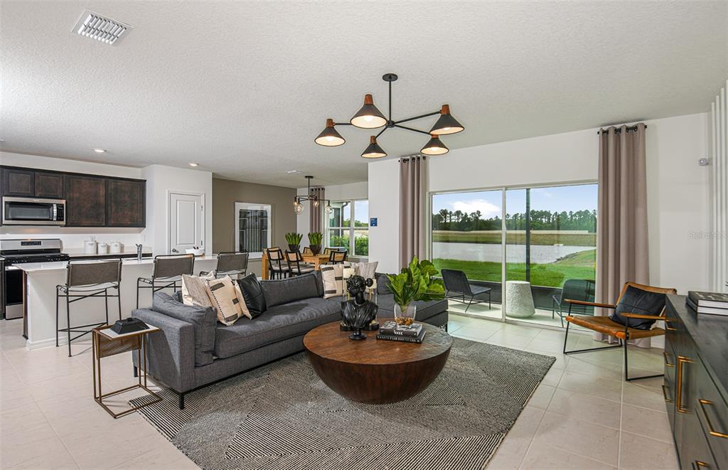 An open-concept living room and kitchen featuring a gray sectional, round coffee table, and patio — 9885 TRELLIS VINE WAY, PARRISH, FL