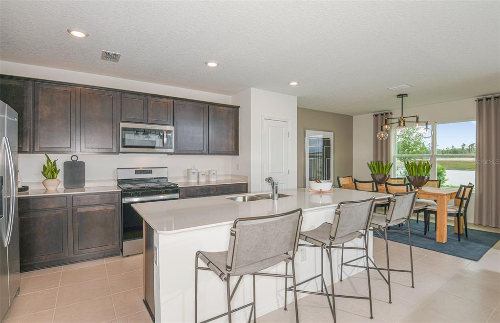 A kitchen with dark wood cabinets, a white island, and an adjacent dining area — 9885 TRELLIS VINE WAY, PARRISH, FL