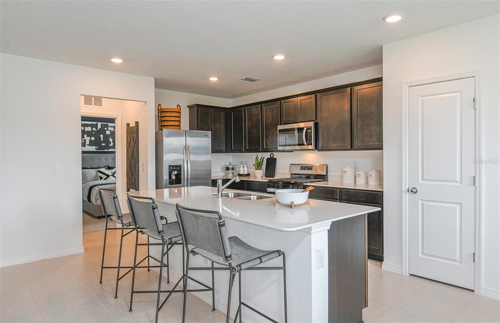 A kitchen with dark cabinets, a white island, stainless steel appliances, and tile flooring — 9885 TRELLIS VINE WAY, PARRISH, FL