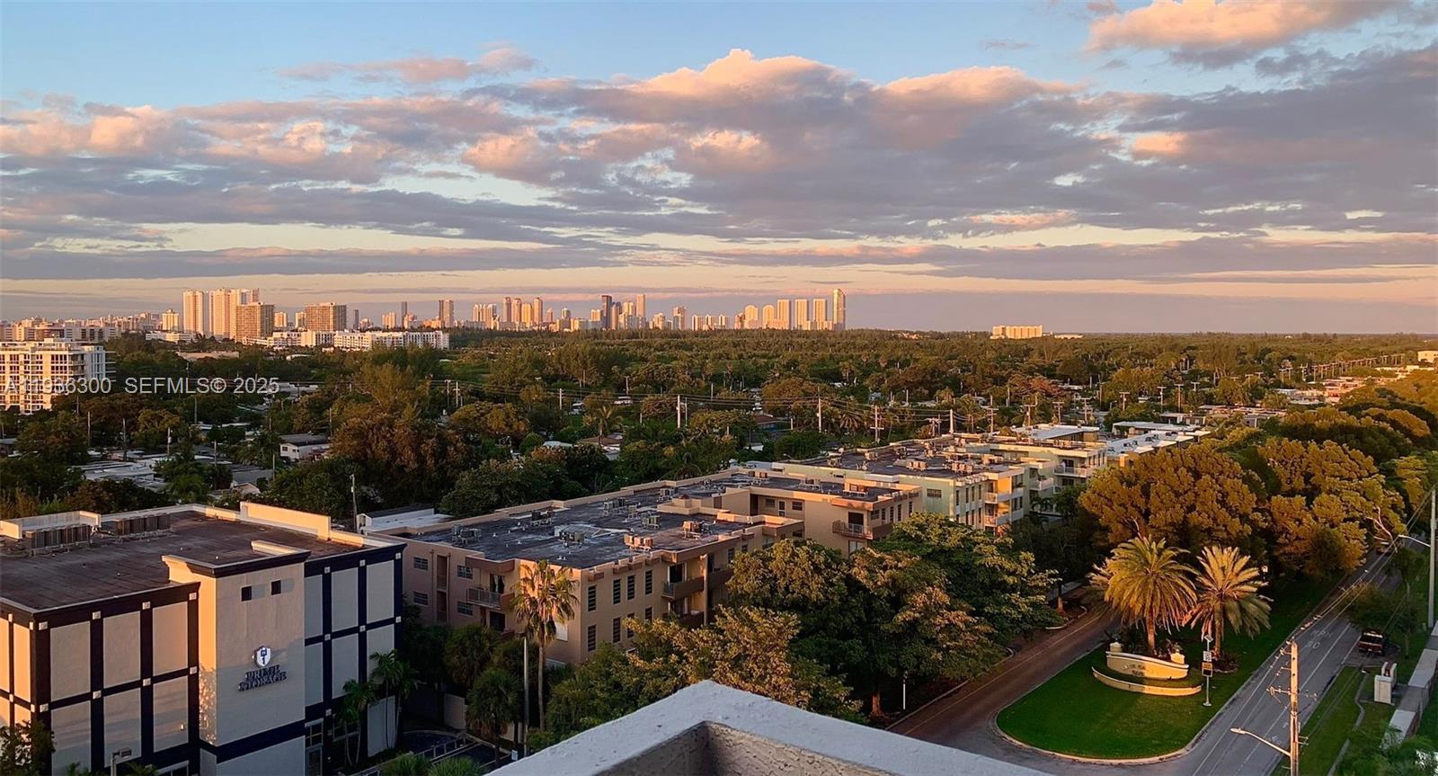 An elevated view shows a suburban landscape with apartment buildings, trees, and a distant skyline — 13499 Biscayne Blvd # 1013, North Miami FL 33181, NORTH MIAMI, FL