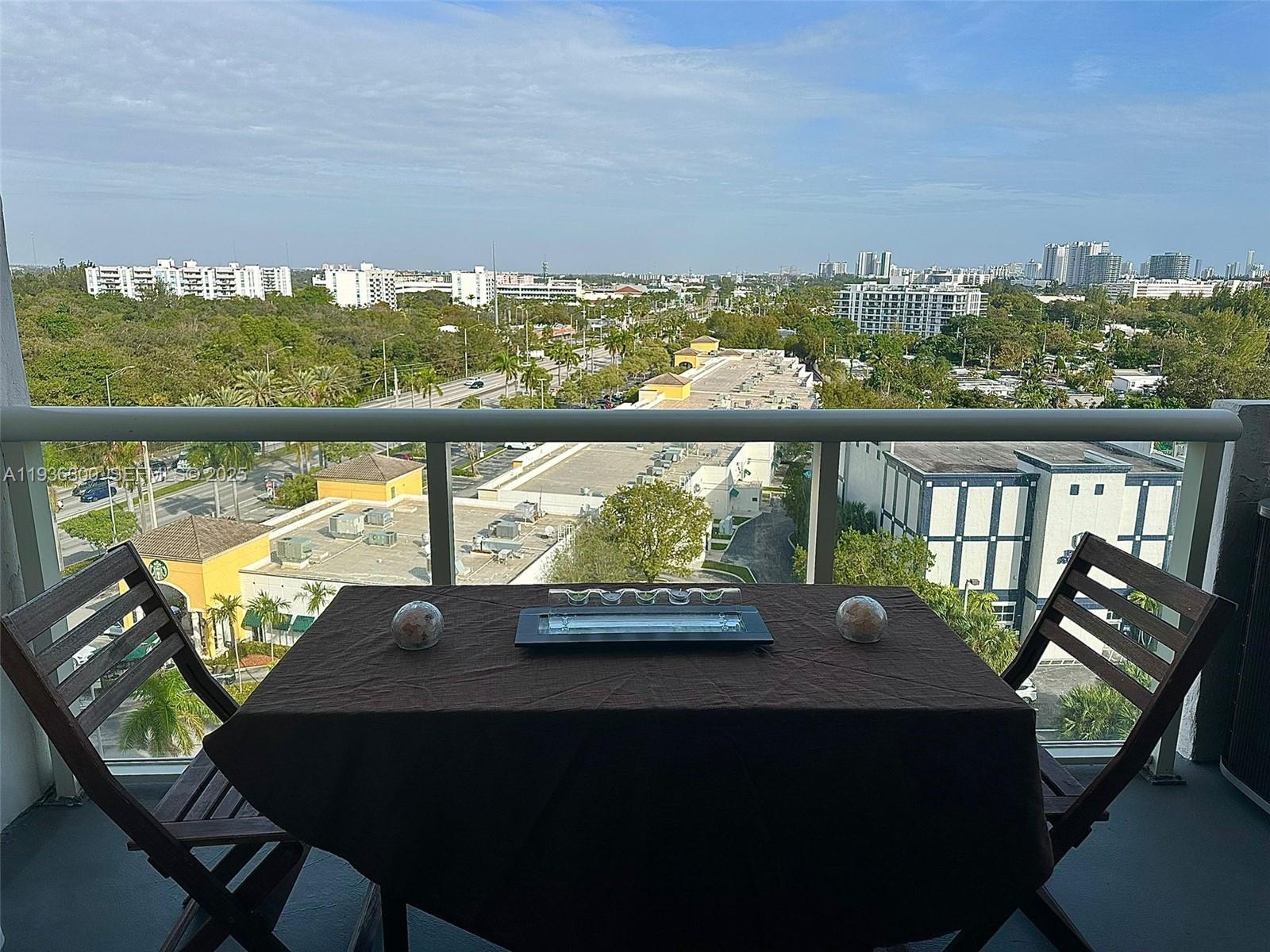 A balcony features a small table with two chairs overlooking a suburban city landscape — 13499 Biscayne Blvd # 1013, North Miami FL 33181, NORTH MIAMI, FL