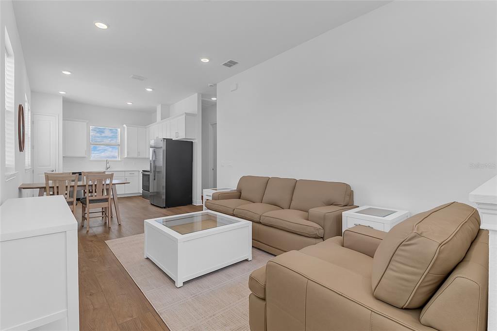 A living room with tan leather furniture and a coffee table opens to a kitchen — 9687 MACBRIDE DRIVE, ORLANDO, FL