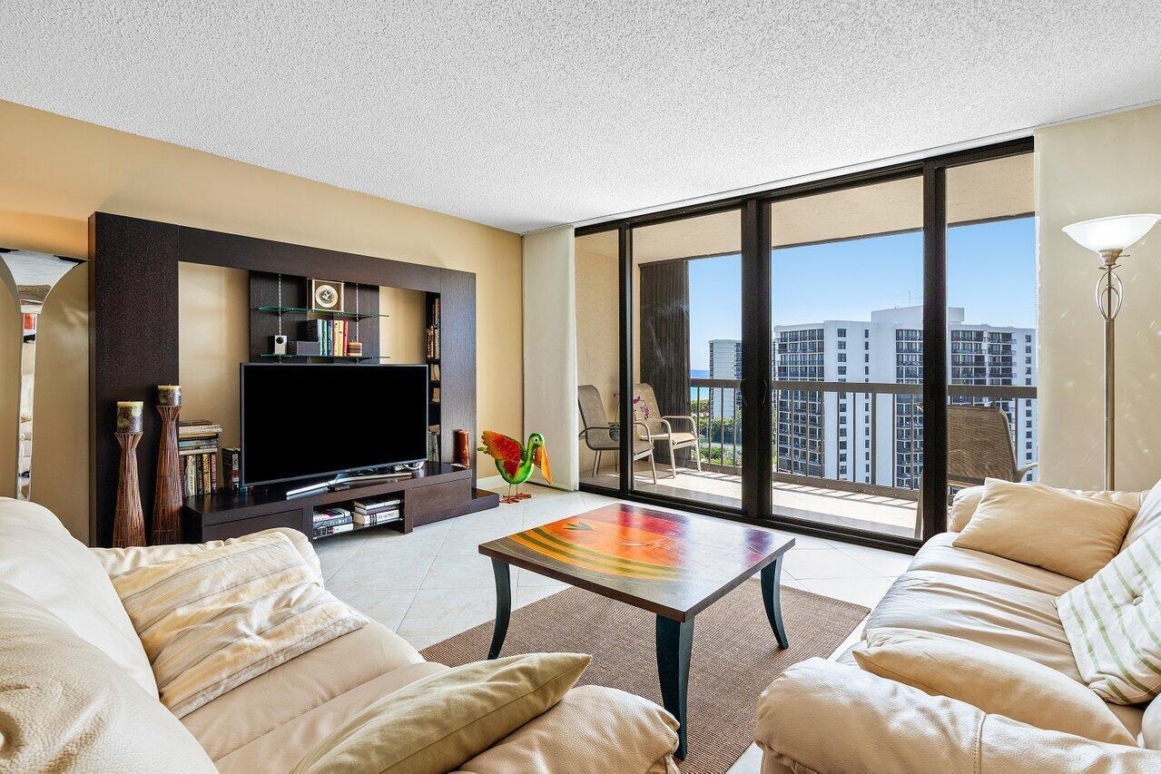 A living room features a dark entertainment center, beige sofas, a coffee table, and balcony views — 4740 S Ocean Boulevard # 1515, Highland Beach FL 33487, HIGHLAND BEACH, FL