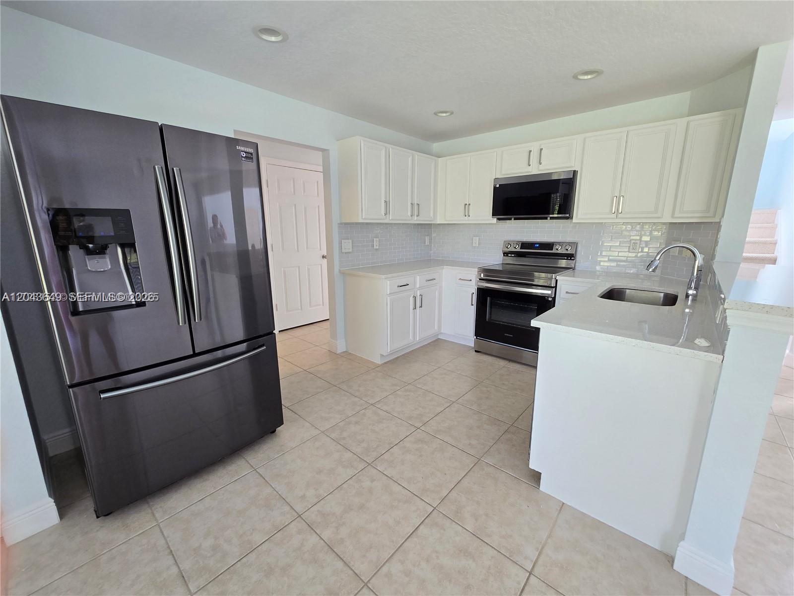 A kitchen features white cabinets, stainless steel appliances, a gray refrigerator, and light tile flooring — 4670 SE Graham Dr, Stuart FL 34997, STUART, FL