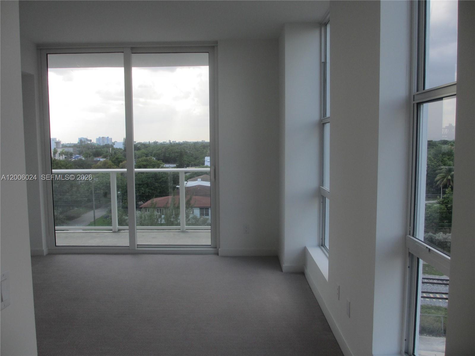 An empty room features gray carpeting, white walls, floor-to-ceiling windows, and a glass balcony door — 4250 Biscayne Blvd # 610, Miami FL 33137, MIAMI, FL