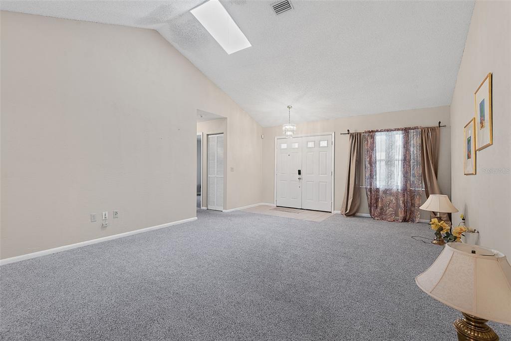 A living room with gray carpet, vaulted ceilings, a skylight, and a double front door — 30 PRINCESS ROSE DRIVE, PALM COAST, FL