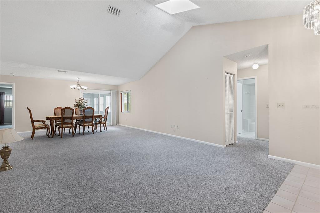 A spacious living and dining area with vaulted ceilings, gray carpeting, and a sliding glass door — 30 PRINCESS ROSE DRIVE, PALM COAST, FL