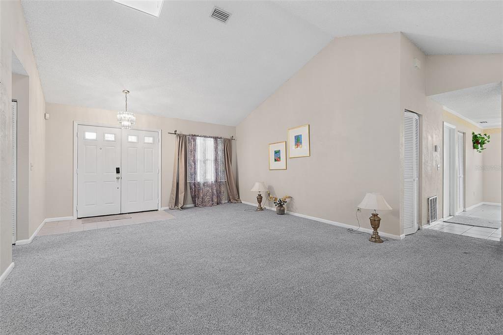 A spacious living room features vaulted ceilings, gray carpeting, a double-door entrance, and two lamps — 30 PRINCESS ROSE DRIVE, PALM COAST, FL