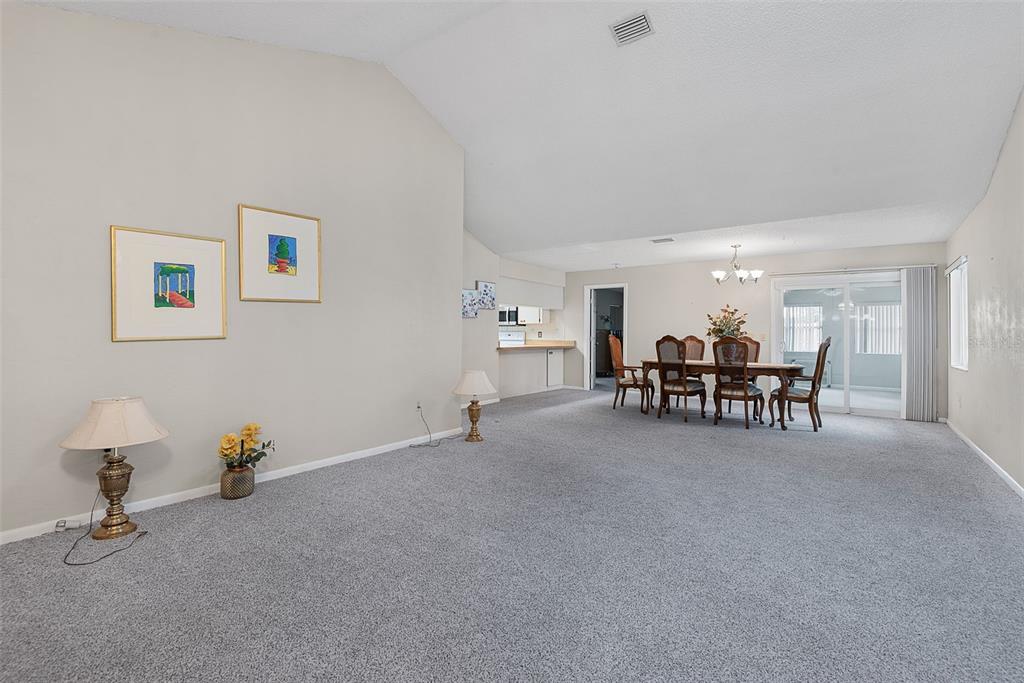 A spacious living and dining area with gray carpeting, vaulted ceilings, and a sliding glass door — 30 PRINCESS ROSE DRIVE, PALM COAST, FL