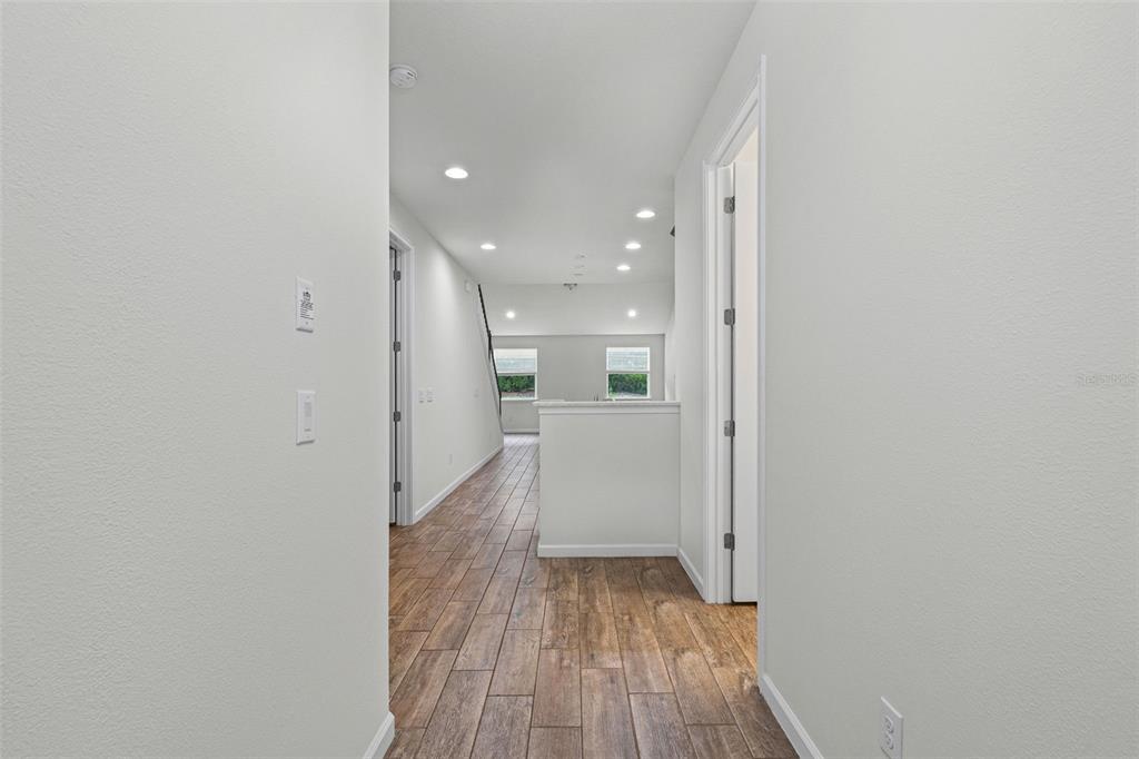 A hallway with wood-look tile flooring leads toward an open living area with windows — 5248 BLOSSOM COVE, BRADENTON, FL