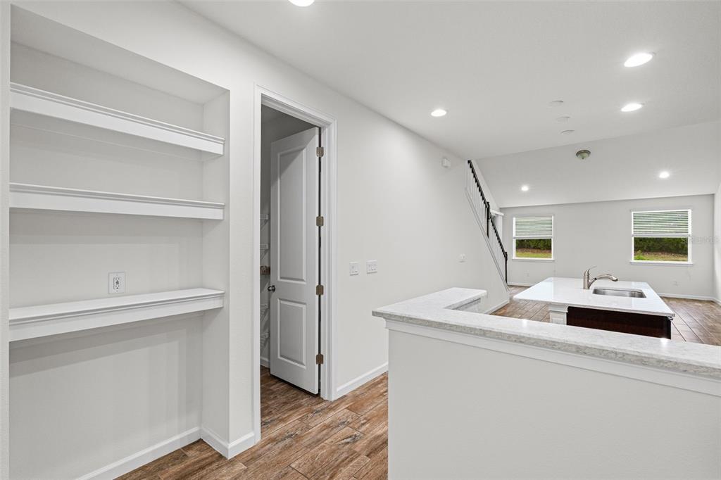 A white kitchen features a granite-topped island, built-in wall shelving, and wood-look flooring — 5248 BLOSSOM COVE, BRADENTON, FL