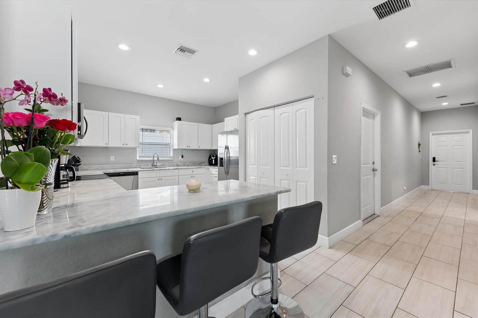 A kitchen features white cabinets, marble countertops, a breakfast bar with stools, and tile flooring — 525 NW 12th Avenue, Boynton Beach FL 33435, BOYNTON BEACH, FL
