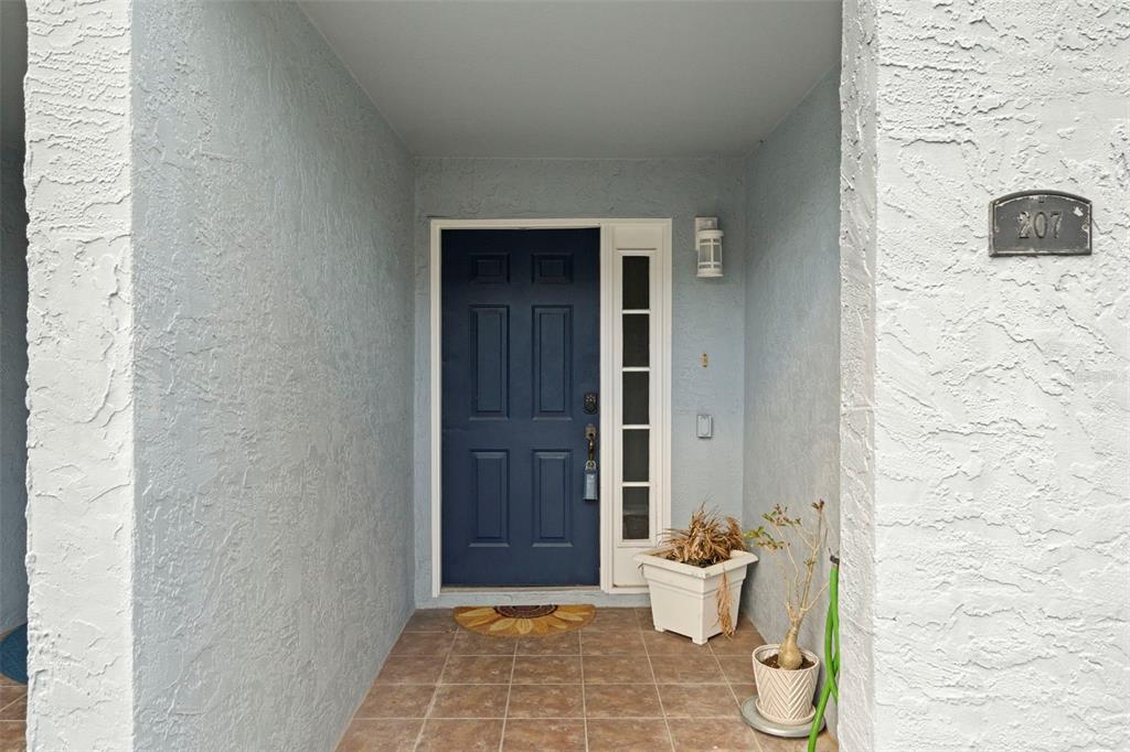A blue front door with a side light sits in a covered entryway with tile — 545 PINELLAS BAYWAY S UNIT 207, TIERRA VERDE, FL