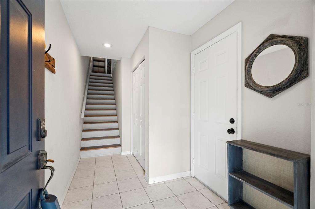 An entryway features tiled flooring, a staircase, a white door, and a wall-mounted mirror — 545 PINELLAS BAYWAY S UNIT 207, TIERRA VERDE, FL
