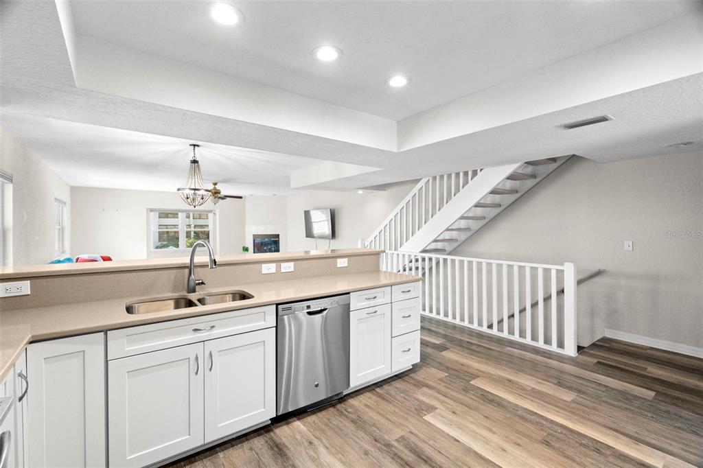 A kitchen with white cabinets and stainless steel appliances overlooks a living area and staircase — 545 PINELLAS BAYWAY S UNIT 207, TIERRA VERDE, FL