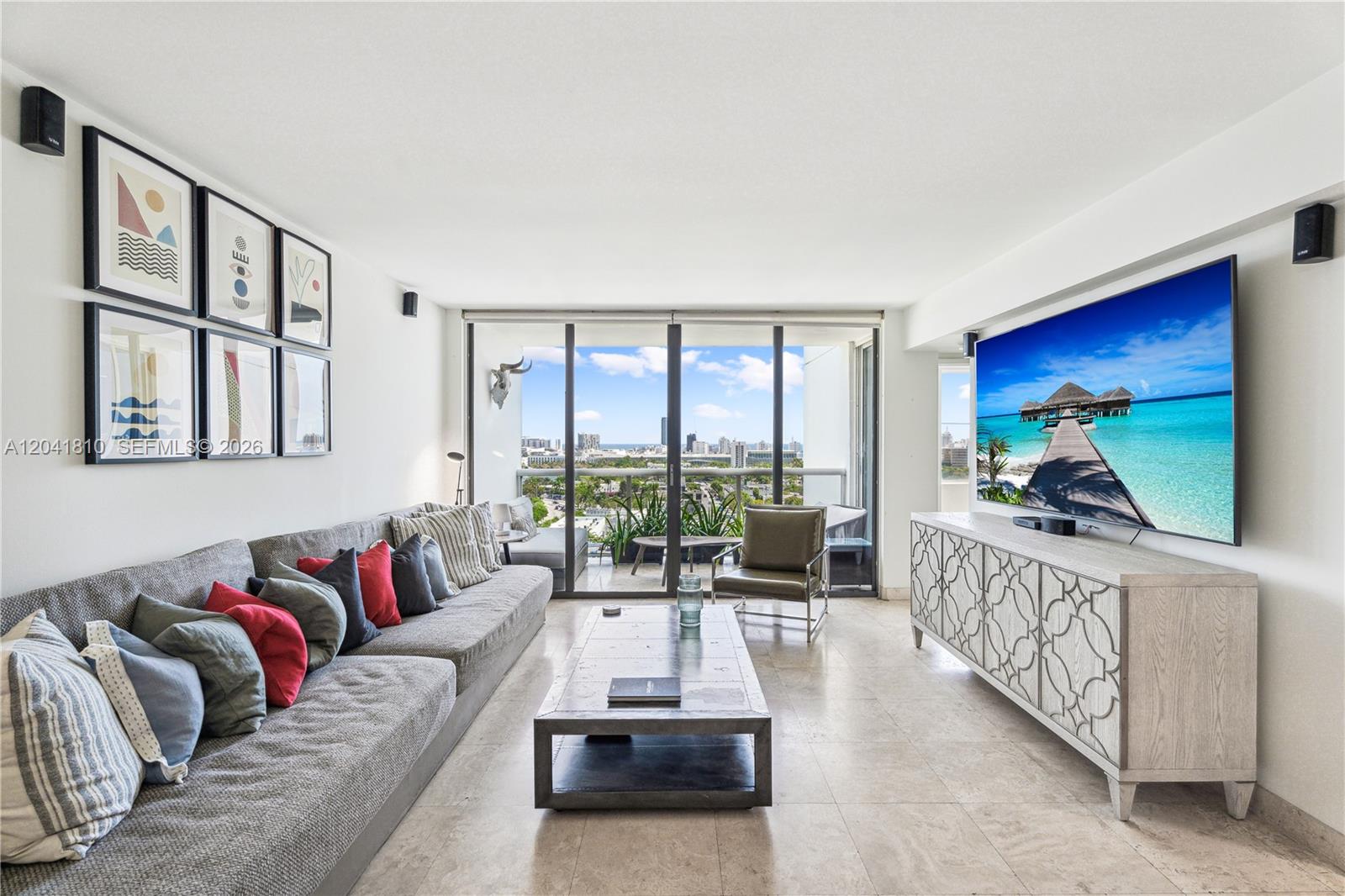 A modern living room features a grey sectional sofa, a large television, and a balcony view — 1900 Sunset Harbour Dr # 1715, Miami Beach FL 33139, MIAMI BEACH, FL