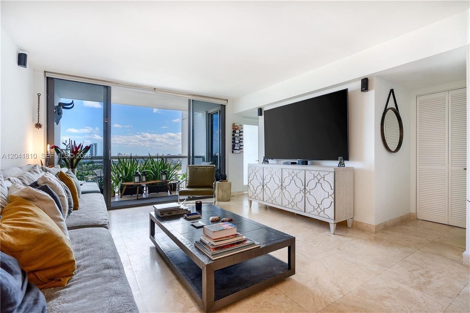 A living room features a large television, a patterned console, and a balcony with plants — 1900 Sunset Harbour Dr # 1715, Miami Beach FL 33139, MIAMI BEACH, FL