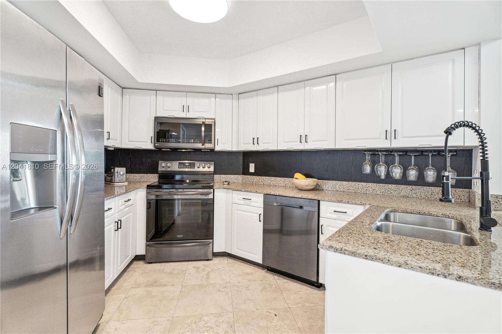 A kitchen features white cabinets, stainless steel appliances, granite countertops, and a black backsplash — 1900 Sunset Harbour Dr # 1715, Miami Beach FL 33139, MIAMI BEACH, FL