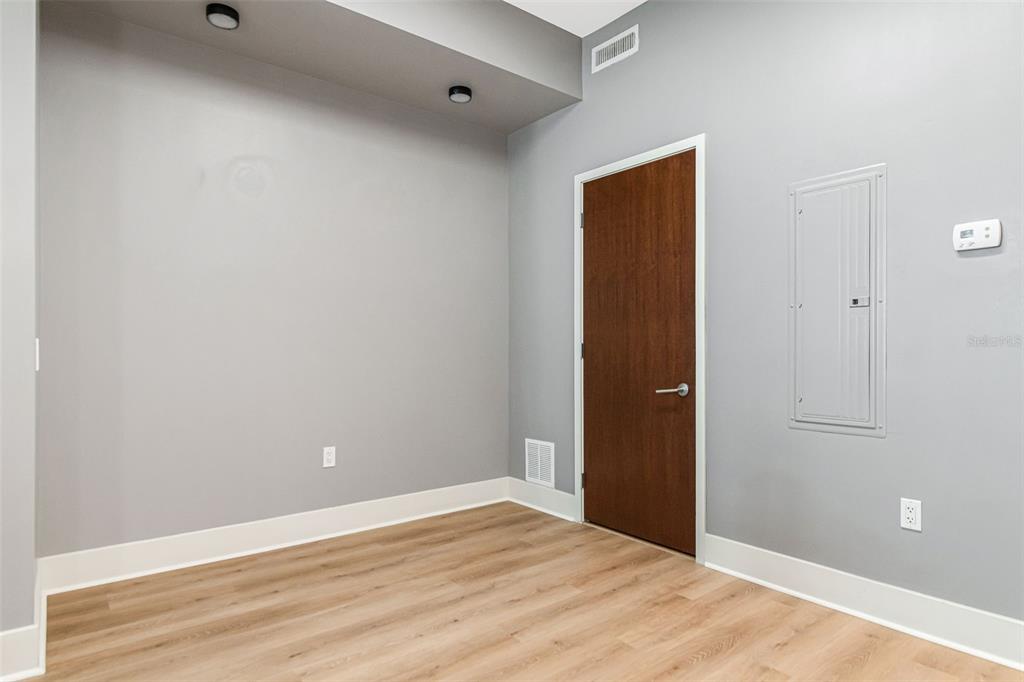 An empty room with light wood-look flooring, gray walls, a brown door, and a breaker panel — 111 N 12TH STREET UNIT 1820, TAMPA, FL