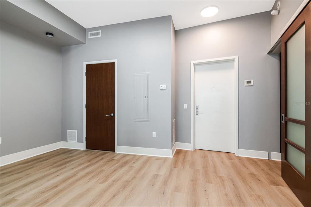 An interior room with light wood-look flooring, gray walls, a dark door, and a white door — 111 N 12TH STREET UNIT 1820, TAMPA, FL