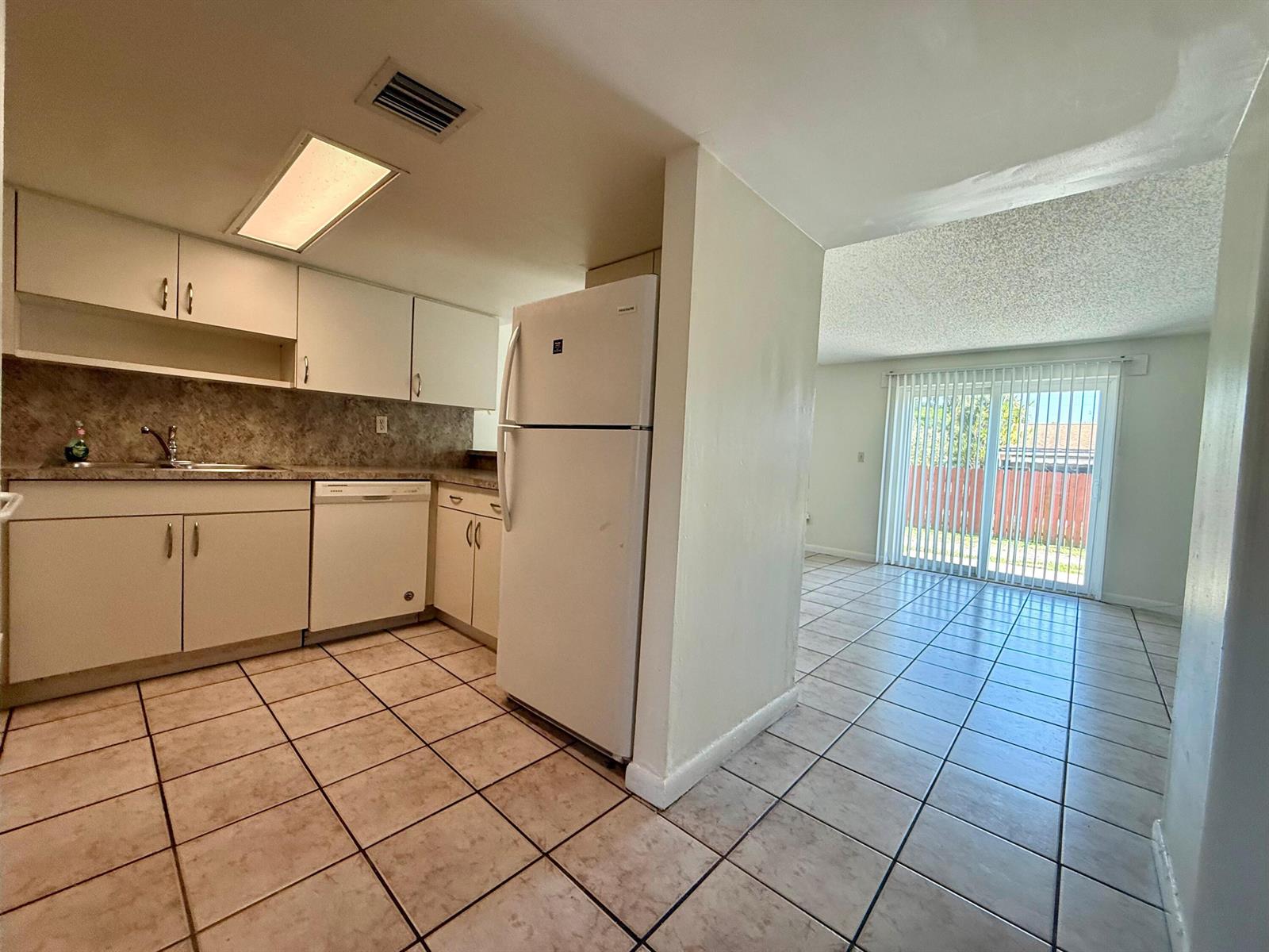 A kitchen with white cabinets and appliances opens into a tiled dining area with sliding doors — 323 Gulfstream Road, Dania Beach FL 33004, DANIA BEACH, FL