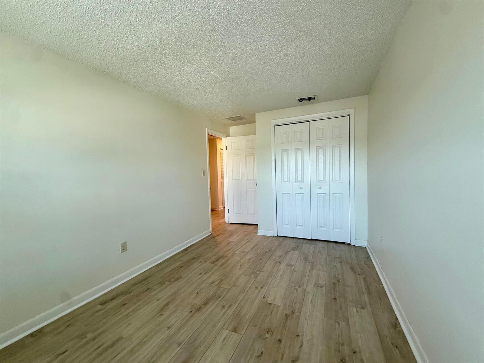 An empty bedroom features light-colored walls, wood-look flooring, and a white closet with double doors — 323 Gulfstream Road, Dania Beach FL 33004, DANIA BEACH, FL