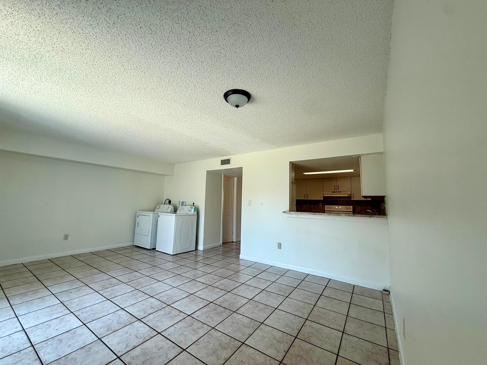 An open-concept room with tile flooring, a laundry area, and a kitchen pass-through window — 323 Gulfstream Road, Dania Beach FL 33004, DANIA BEACH, FL