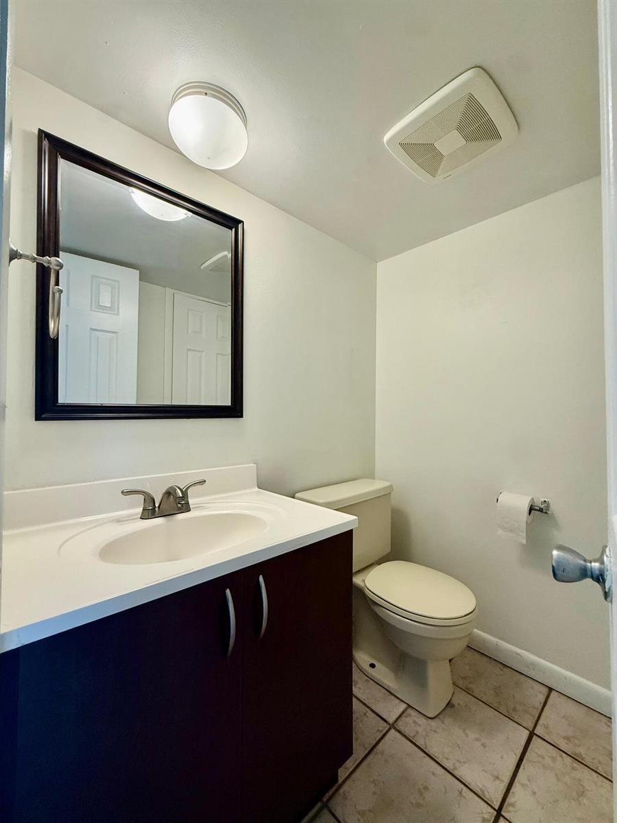 A small bathroom features a dark wood vanity, white countertop, toilet, and a framed mirror — 323 Gulfstream Road, Dania Beach FL 33004, DANIA BEACH, FL