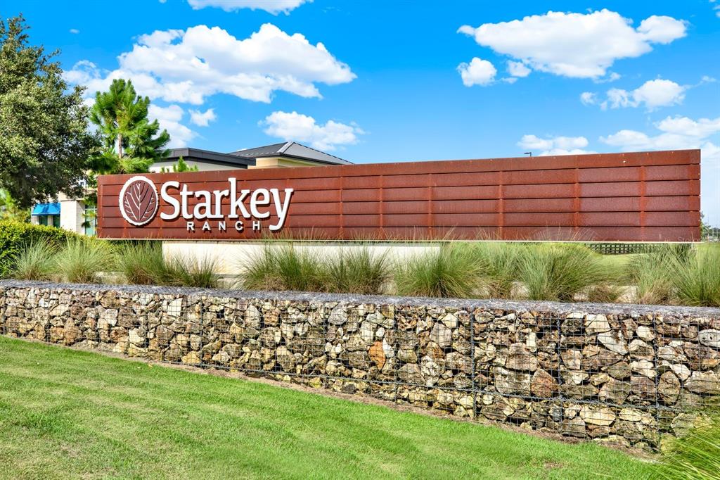 A large metal sign with the Starkey Ranch logo sits behind a stone gabion wall — 13729 RANGELAND BOULEVARD, ODESSA, FL