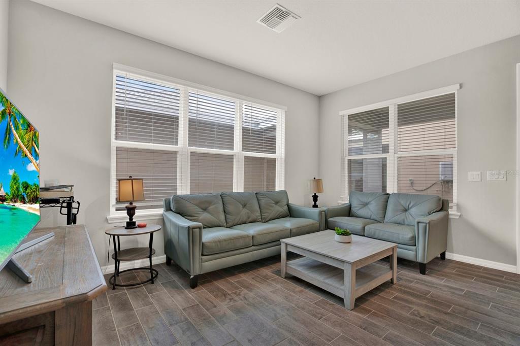 A living room features a grey sofa and loveseat, a coffee table, and wood-look tile flooring — 13729 RANGELAND BOULEVARD, ODESSA, FL