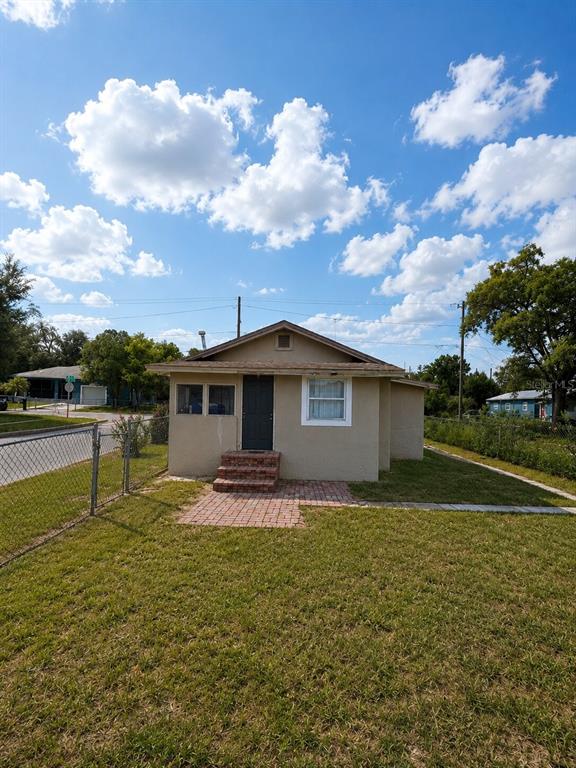 A small, tan, single-story house with a brick stoop and a chain-link fence — 1239 AVENUE K, HAINES CITY, FL