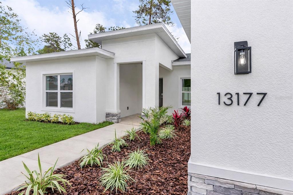 A modern white stucco house exterior features a covered entryway, stone accents, and landscaping — 13177 SW 67TH AVENUE, OCALA, FL